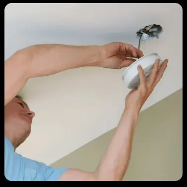 A man installs a smoke detector to the ceiling