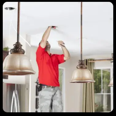 A man in a red shirt installs a light fixture