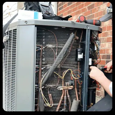 An HVAC technician is repairing a gray AC unit outside