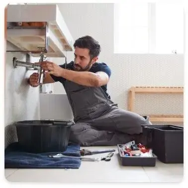 A plumber is repairing a sink, kneeling with tools nearby