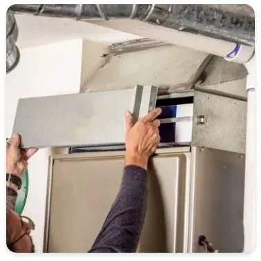 A person removes an access panel to check an HVAC system filter