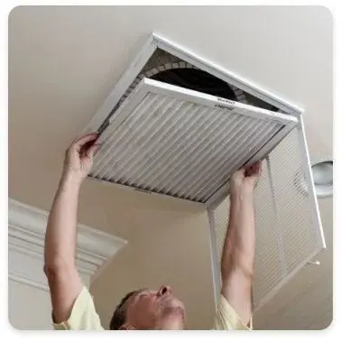 A person opens an air intake vent in a ceiling to replace the air filter